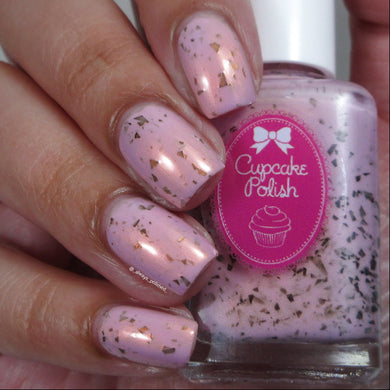 Hand with pink speckled nail polish holding a bottle of Cupcake Polish.