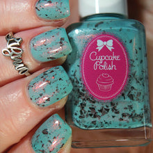 Turquoise nail polish with glitter held by a hand, featuring Cupcake Polish brand.