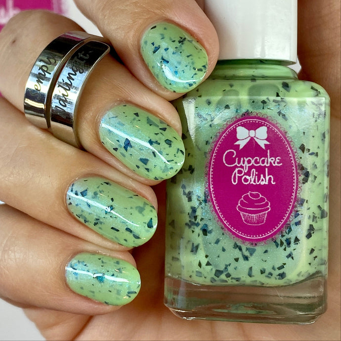 Hand with green speckled nail polish holding a bottle of Cupcake Polish.